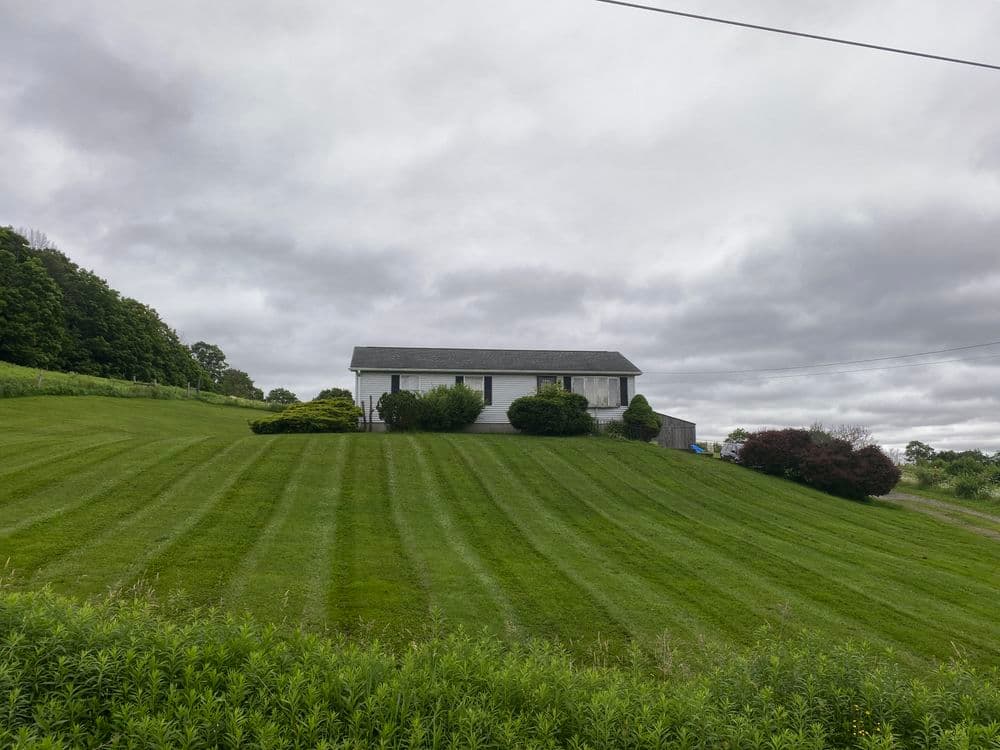 Single-story house on a green hillside with neatly striped lawn and overcast sky.