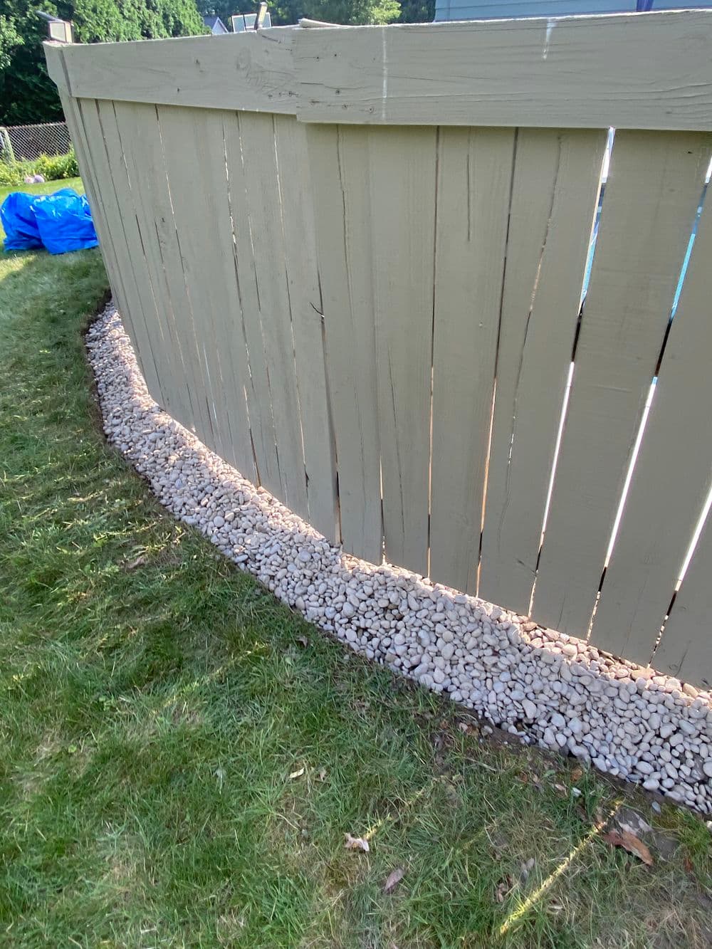 Curved wooden fence with gravel landscaping along the base on a grassy area.