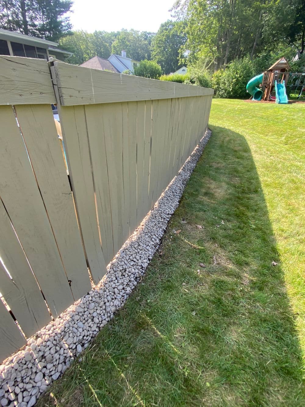 Wooden fence with gravel border along a grassy area and children's play set.