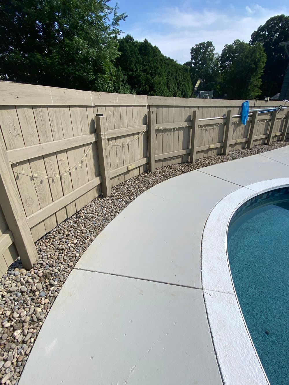 Wooden fence surrounding a pool area with decorative lights and landscaped gravel.