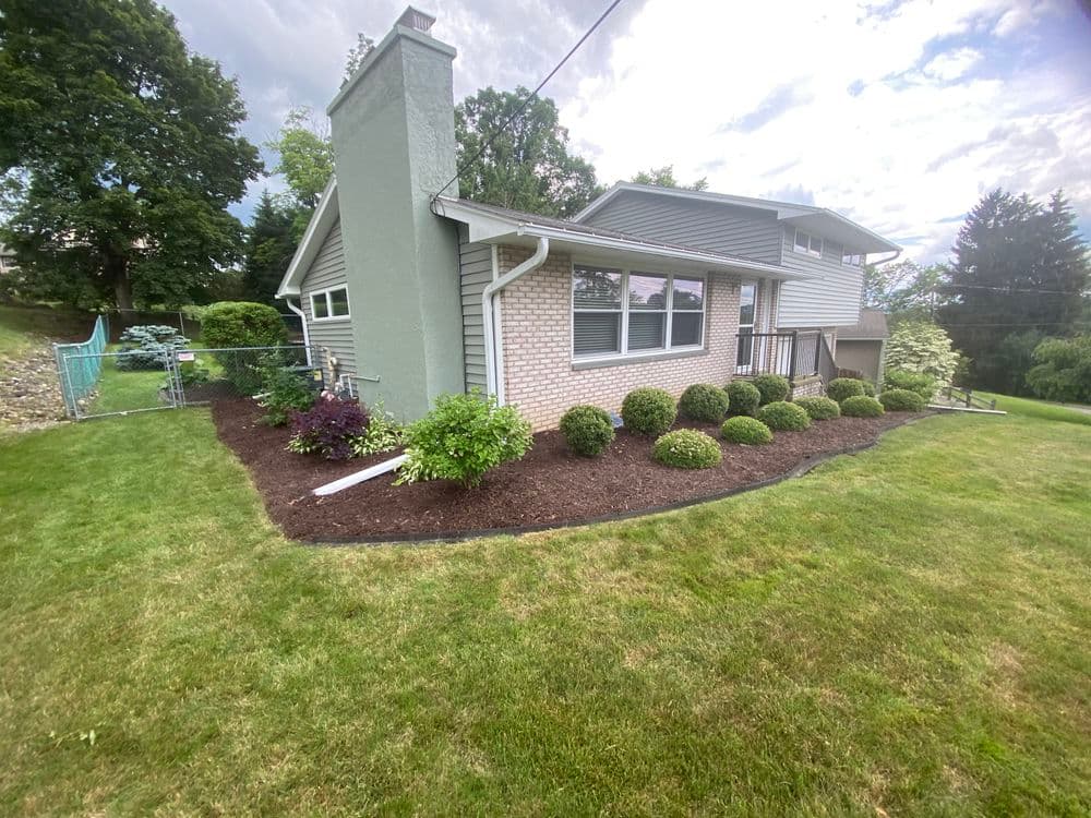 Modern home with landscaped yard, featuring shrubs and a stone chimney under cloudy sky.