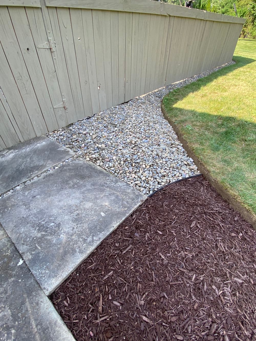 Pathway design featuring gravel, mulch, and a concrete slab alongside a wooden fence.