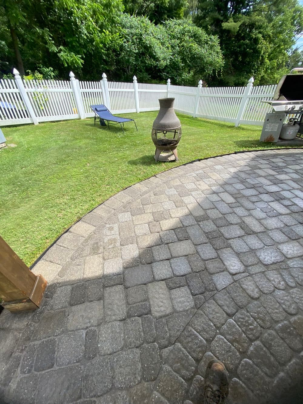 Outdoor patio with a stone walkway, chiminea, lawn chair, and a white picket fence.