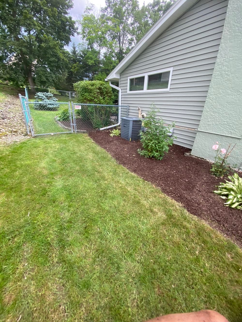 Lush green lawn with flower beds and a fence surrounding a house's side yard.