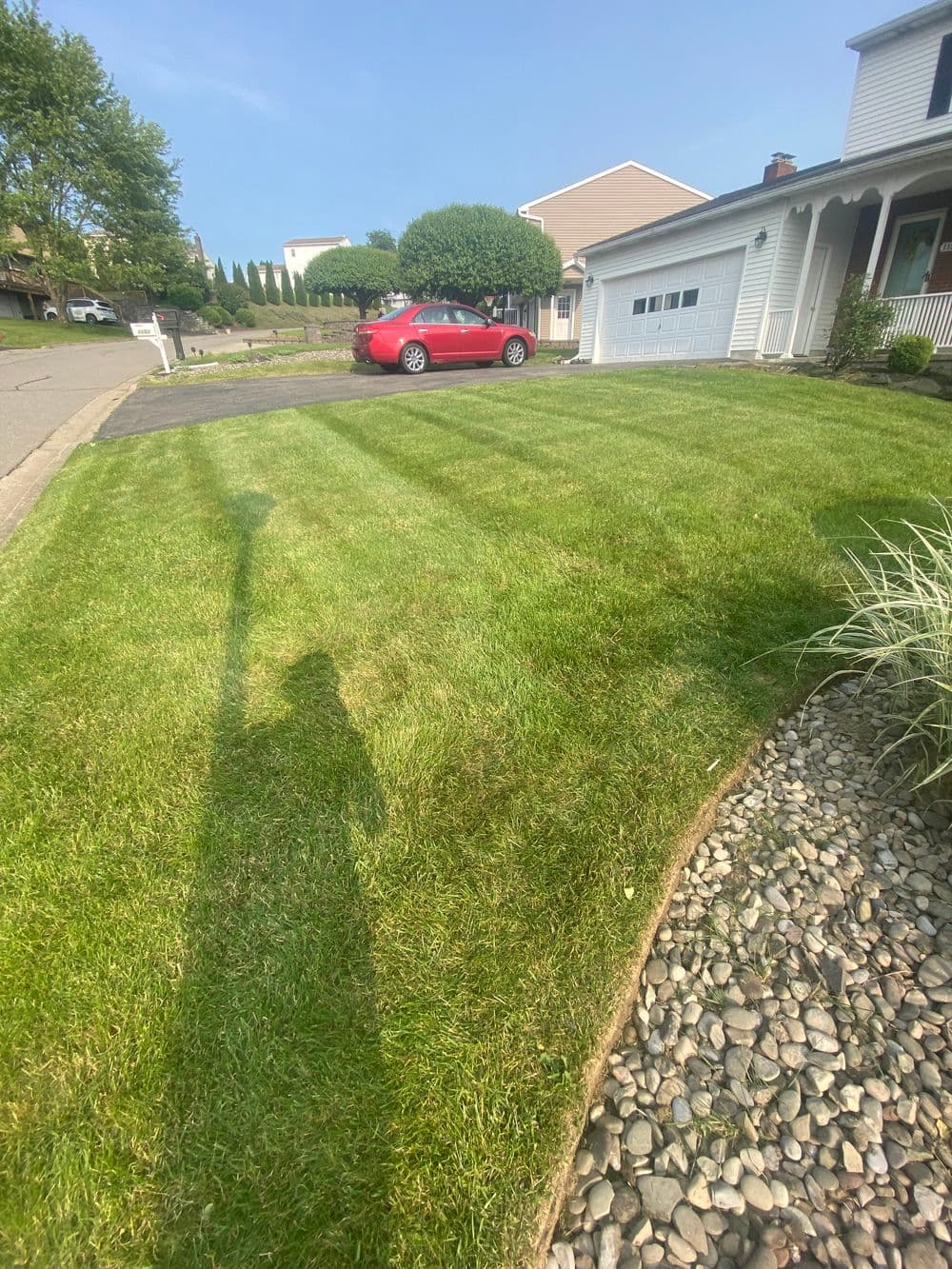 Lush green lawn with striped pattern, driveway, and red car parked near a house.